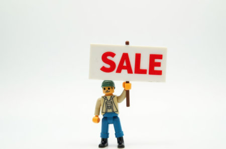 toy man holding a sign with the text Sale on a white backgroundの素材