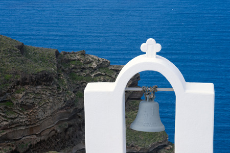 Santorini, Greece, April 2019. White dome and bell on a background of blue sea, an island and a volcano. Beautiful landscape.の写真素材