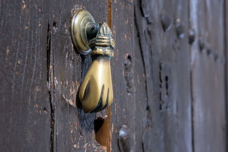 Old bronze door handle in the shape of a hand. Brown wooden door of a house in the Spanish city of Ronda.のeditorial素材