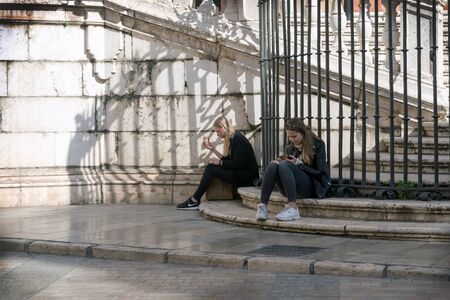 Malaga, Spain, February 2019.Two girls relax on the marble steps of the famous Malagan Incarnate Cathedral and eat ice cream. Malaga Cathedral is the main attraction of the city. Break in the journey.のeditorial素材
