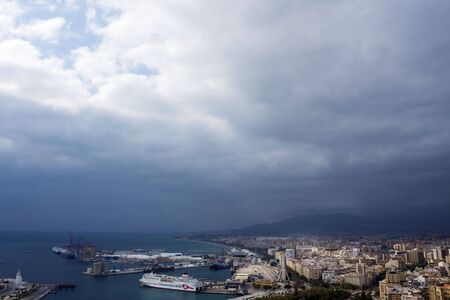 Malaga, Spain, February 2019. Panorama of the Spanish city of Malaga. Buildings, port, bay, ships and mountains against a cloudy sky. Dramatic sky over the city.のeditorial素材