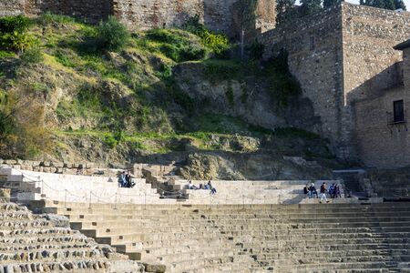 Malaga, Spain, February 2019. Roman theater on the background of the Alcazaba. People relax on stone benches for spectators on a warm sunny day. Ruin.のeditorial素材