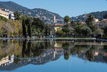 Nice, France, March 2019. Fountain on the embankment du Pillon on a warm sunny day. Reflection of the city in the water. Walk on the Cote d'Azur.のeditorial素材