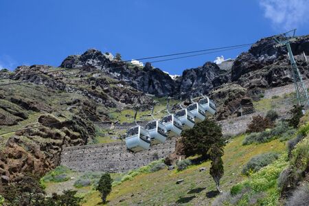 Santorini, Greece, April 2019. Tourists in the cabins of the cable car rise from the old port of Santorini. Beautiful view of the mountains, covered with wildflowers.のeditorial素材