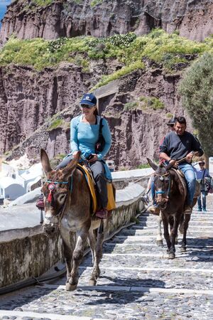 Santorini, Greece, April 2019. Tourists on a brown horse against the blue sky and island. Climb the stairs from the old port on a sunny day.のeditorial素材