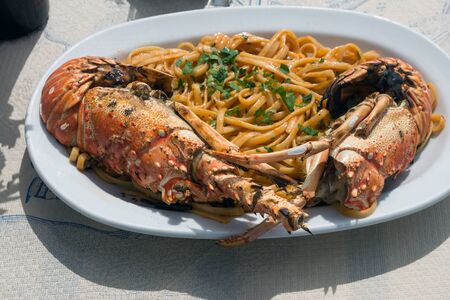Delicious lunch by the sea. A white plate of spaghetti with huge lobsters on the grill. Travel to Santorini, Greece. Old port of Fira.の写真素材