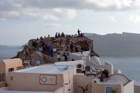 Santorini, Greece, April 2019. White traditional Greek houses on a hillside on the island of Santorini. Tourists are waiting for sunset. Sunset in the city of Oia, Santorini.のeditorial素材