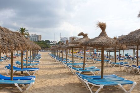 Magaluf, Mallorca, July 2019. Mallorca traditional thatched umbrellas and blue sunbeds on the sandy beach of Magaluf resort. Balearic Islands.のeditorial素材