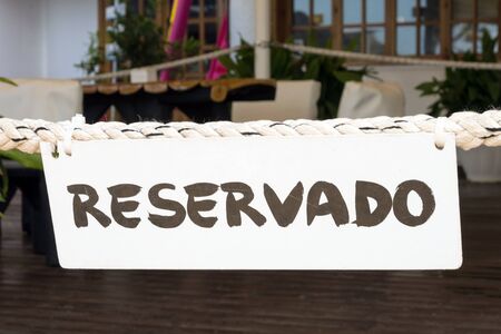 On a thick rope in a Spanish restaurant on the island of Mallorca is a white Reservado sign. The restaurant is closed for special services. VIP guests.の写真素材