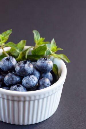 Big tasty blueberry and green mint leaves in a white plate on a dark background. Healthy berry. Vaccinium uliginosum.の写真素材