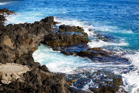 Waves beat against stones of volcanic origin on the island of San Miguel, Azores. Seascape. Travel.