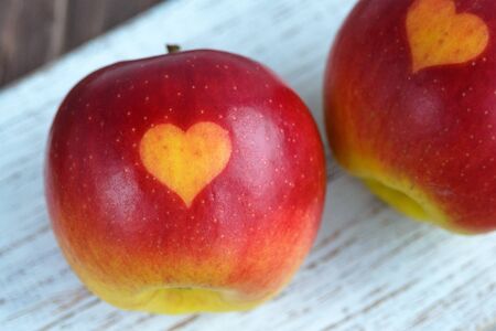 Two red apples with a heart seal on the table. Orange heart on organically grown fruits. Growing...