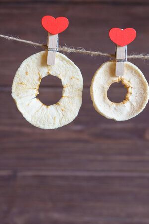 Red heart-shaped clothespins contain fruit chips. Dried organic apple fitness chips on a dark background. A popular tasty and fresh healthy product. A healthy, dietary, low-calorie and tasty snack.の写真素材