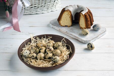 Quail eggs in a brown clay plate on a white wooden background. A closeup. Easter concept.