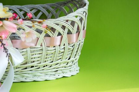 White Easter basket decorated with flowers with a satin ribbon on a green background. Easter concept.の写真素材