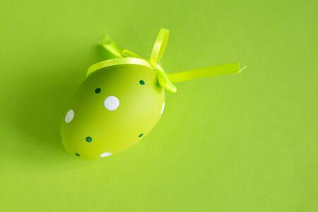 Decorative green egg with a green satin ribbon on a green background. Easter concept.