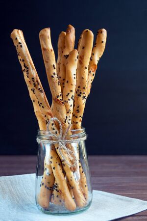 Traditional italian thin crispy grissini sticks with black sesame seeds and cheese in a glass jar on a black background. National cuisine of Italy.の写真素材