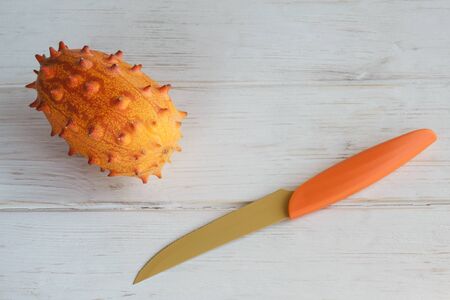 Exotic fruit Cucumis metuliferus, African cucumber and knife on a white wooden background. Closeup, soft focusの写真素材