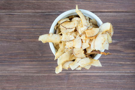 Delicious crispy coconut chips with salted caramel in a white plate on a dark wooden background. Natural product made from coconut pulp. The concept of proper nutrition.の写真素材