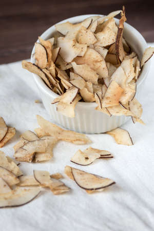 Delicious crunchy coconut chips with salted caramel in a white plate on a white breezy cloth. Natural product made from coconut pulp. Useful snack for a snack. The concept of proper nutrition.の写真素材