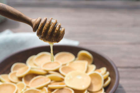 Wooden spoon for honey close-up. Drops of honey flow down on traditional american breakfast cereal mini Pancakes.の写真素材