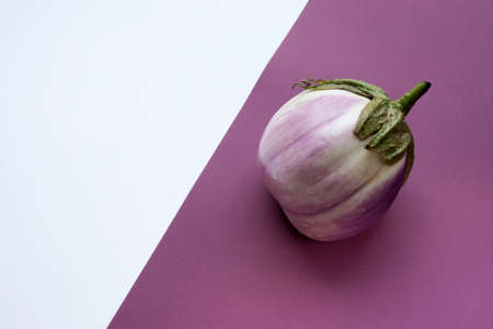 Ugly eggplant on a contrasting white and purple paper background. Organic vegetable Solanum melongena. Conscious eating concept.の写真素材