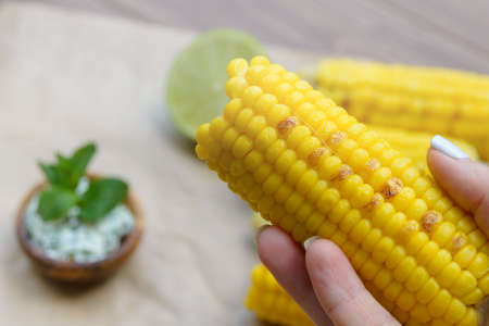 Young yellow fried sweet corn in the girl's hand. Delicious summer food. Close-up.の写真素材