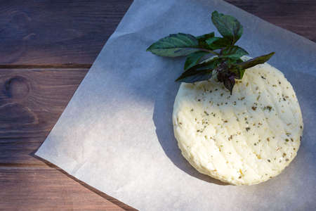 Fresh salted Levantine halloumi cheese and a sprig of basil on a brown wooden background....