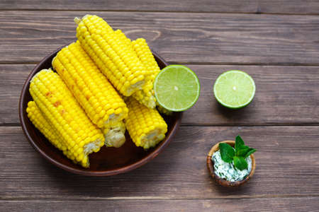 Young sweet tasty grilled corn with spicy lime oil in a clay plate on a wooden dark background. Summer food.の写真素材