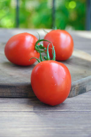 Three large red tomatoes on a wooden board. Ripe fruits of Solanum lycopersicum close-up.の写真素材