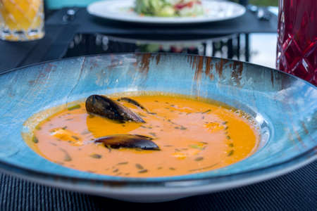 Delicious seafood tomato bouillabaisse fish soup with shrimps, mussels and fish in a blue plate on...