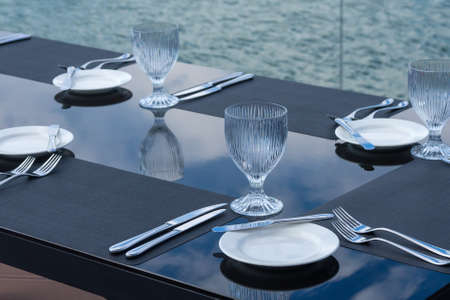 Crystal empty glasses, white plates and cutlery on a table in a beach restaurant. Table setting for...