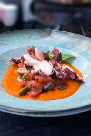 Fried octopus in tomato sauce with olives and capers in a blue plate. Delicious traditional Italian dish. Dinner at a fish restaurant.の写真素材