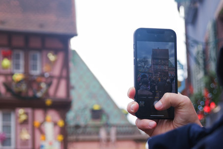 Colmar, France, Alsace, December 2021. The French city of Colmar on the eve of the Christmas holiday. Colorful medieval houses in the city. A man takes a photo of the street with a mobile phone.のeditorial素材
