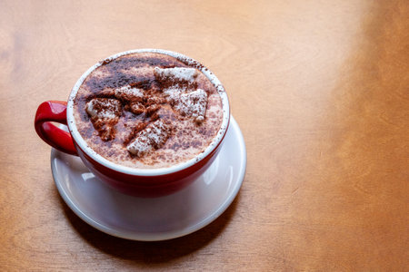 Cocoa with marshmallows in a red cup on a wooden table. Delicious drink.
