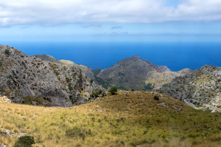 Mountain peaks under a bright sky with lush greenery and blue sea on the horizon. Mallorca island.の写真素材