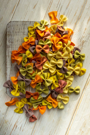 A unique variety of Italian pasta. Multi-colored farfalle with spinach, beets, paprika and carrots on a white wooden background.の写真素材