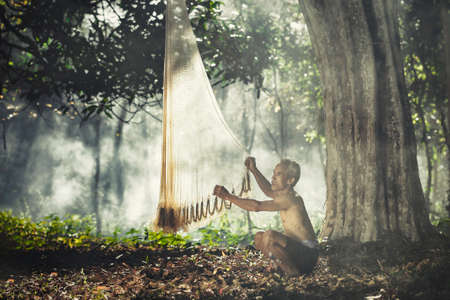SAKONNAKHON, THAILAND â FEBRUARY 5: A white-haired, shirtless old man standing teaching his grandson repairing fishing nets under a big tree on February 5, 2017 in Sakonnakhon, Thailand.のeditorial素材