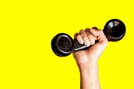 Hand holding old telephone receiver on yellow background.の写真素材
