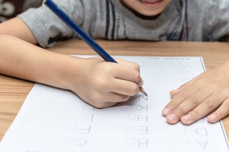 Close up hand writing homework on wooden table at home. Kid learing and writing alphabet.