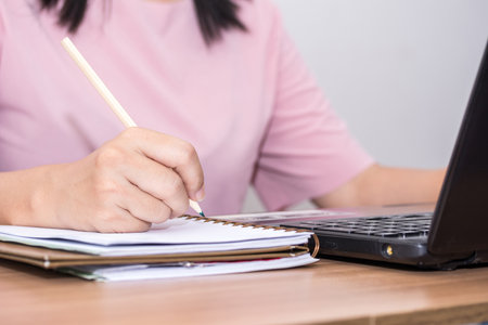 Closeup a woman hand holding pencil and using a laptop computer working at her desk in the office. A...