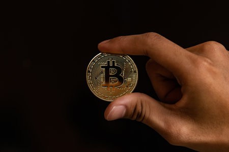 Close up one golden coin with the bitcoin symbol in hand. Young hand holding cryptocurrency coin,...