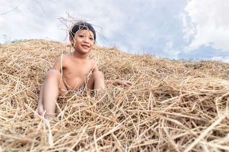 Portrait of a cute little Asian boy smiling and sitting on hay. Little joyful child playing on the rice straw.の写真素材