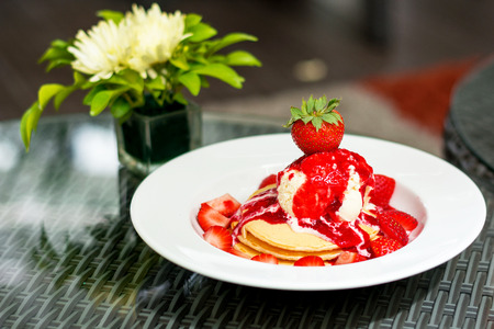 Pancake and ice cream ontop with strawberry into white dish on glass tableの写真素材