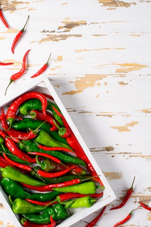 Hot red and green peppers, red chillies in the white wooden box on the old white wooden tableの写真素材