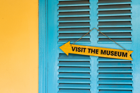Wooden museum sign on blue window shutters next to yellow wallの写真素材
