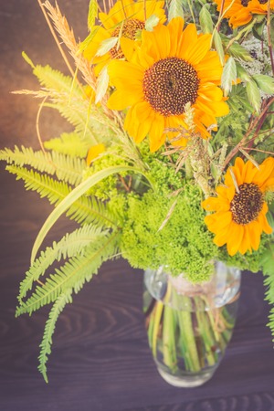 Bouquet of sunflowers in a glass vase on a wooden table.の写真素材