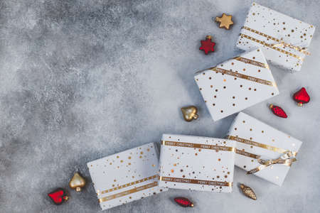 Gift boxes in white paper with stars and dots with golden ribbons on grey background. Flat lay with...