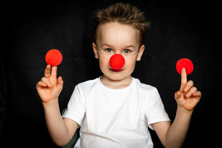 Boy with a clown red nose and red noses in hands. Red Nose Day.