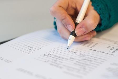 closeup of female hand signing document in blue sweater with black penの写真素材